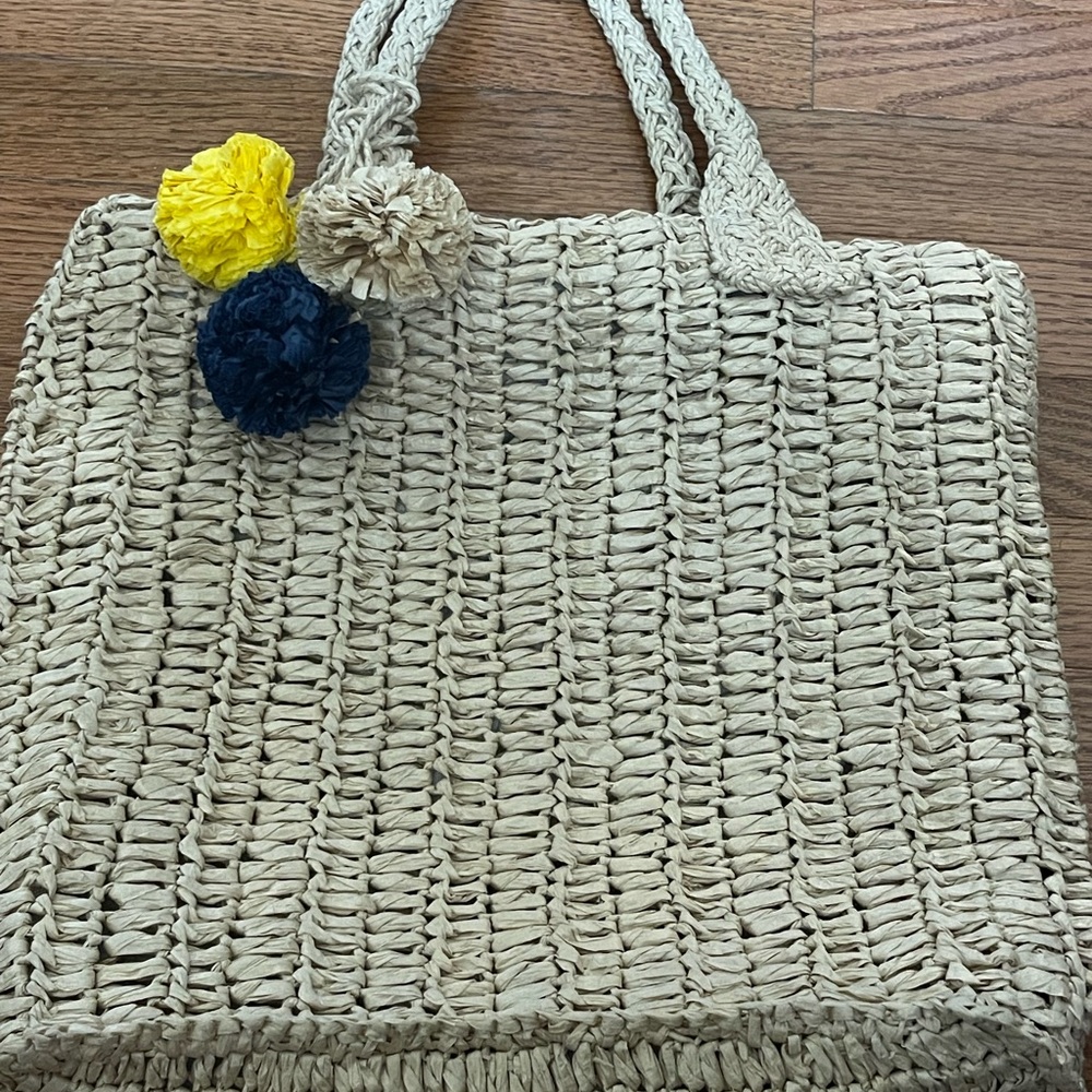 Straw beach bag with 3 different color pom poms.